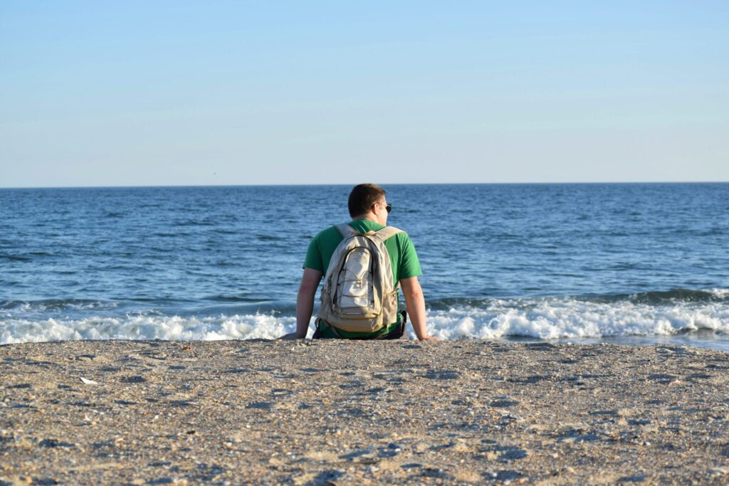 Jeremy Storm sitting on the beach at Fort Macon State Park North Carolina wearing a backpack and overlooking the ocean