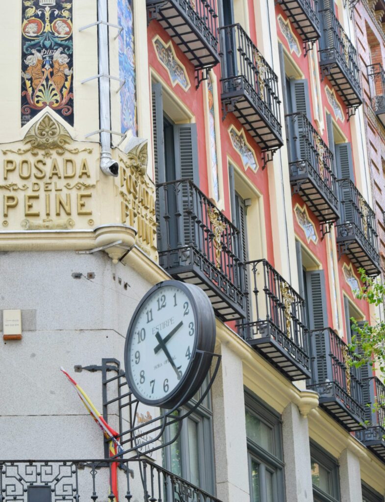 Clock attached to a red building with black wrought iron balconies in Madrid Spain--you'll see plenty of beautiful buildings like this during your 3 days in Madrid!