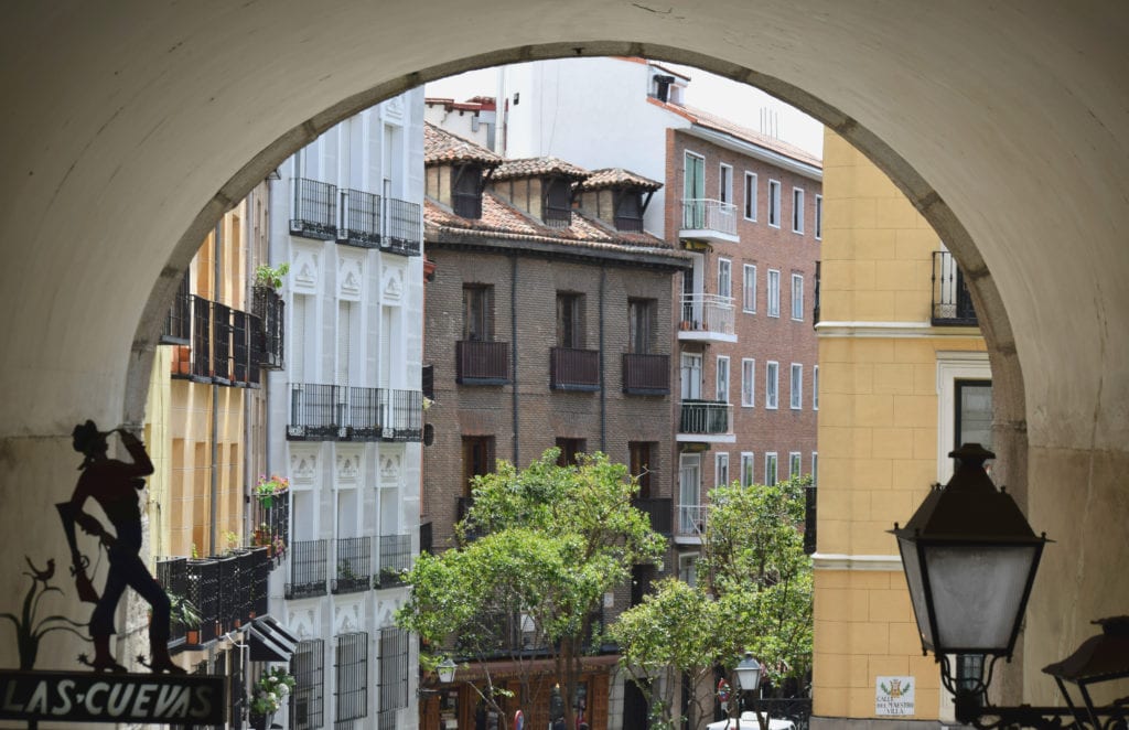 Photo of an arch in Madrid Spain with colorful buildings visible in the background