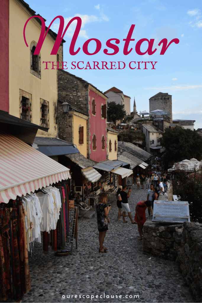 photo of shops in mostar bosnia herzegovina old town, maroon text reads "mostar the scarred city"