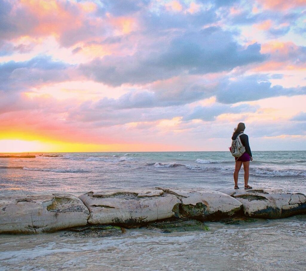 kate storm standing on the beach looking at a sunset on holbox island mexico