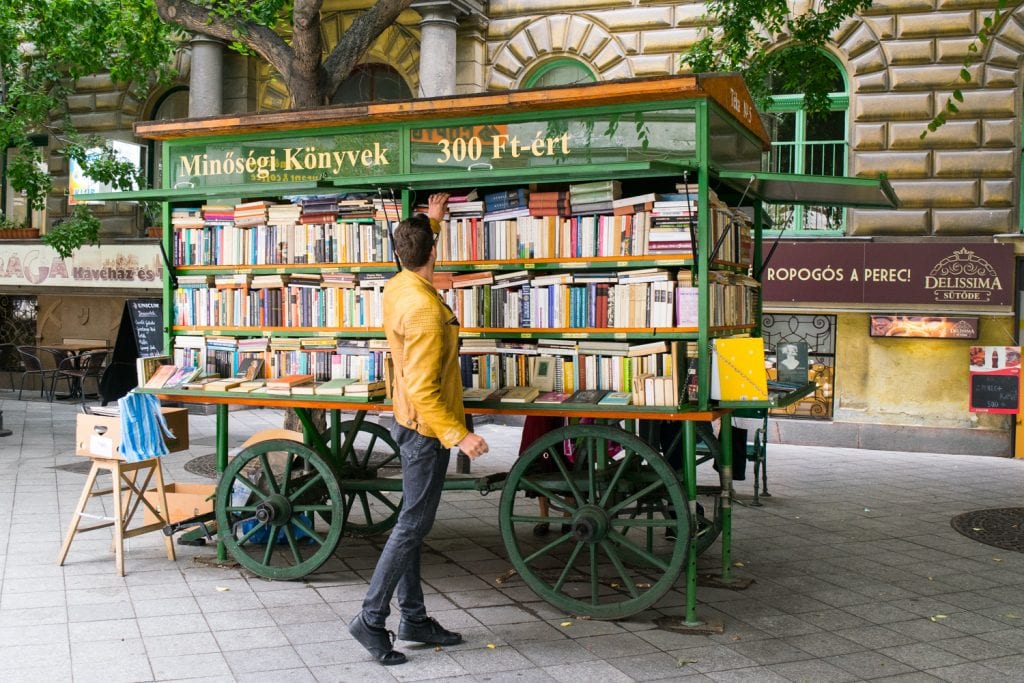 man in a yellow jacket shopping at an outdoor bookstore in budapest, a fairly cheap european destination to visit