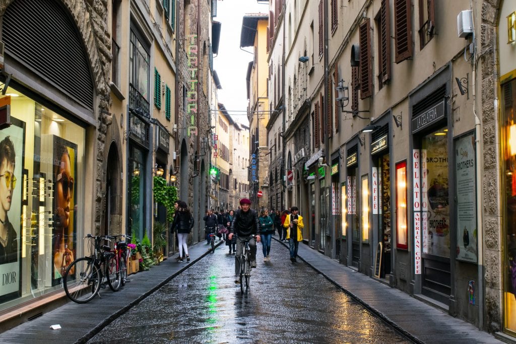 man riding a bike down a cobblestone street in florence italy