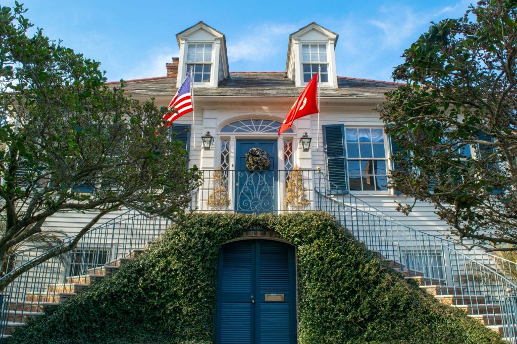 White house in NOLA Garden District with blue doors and American flags hanging out front, as seen during a 3 days in New Orleans itinerary