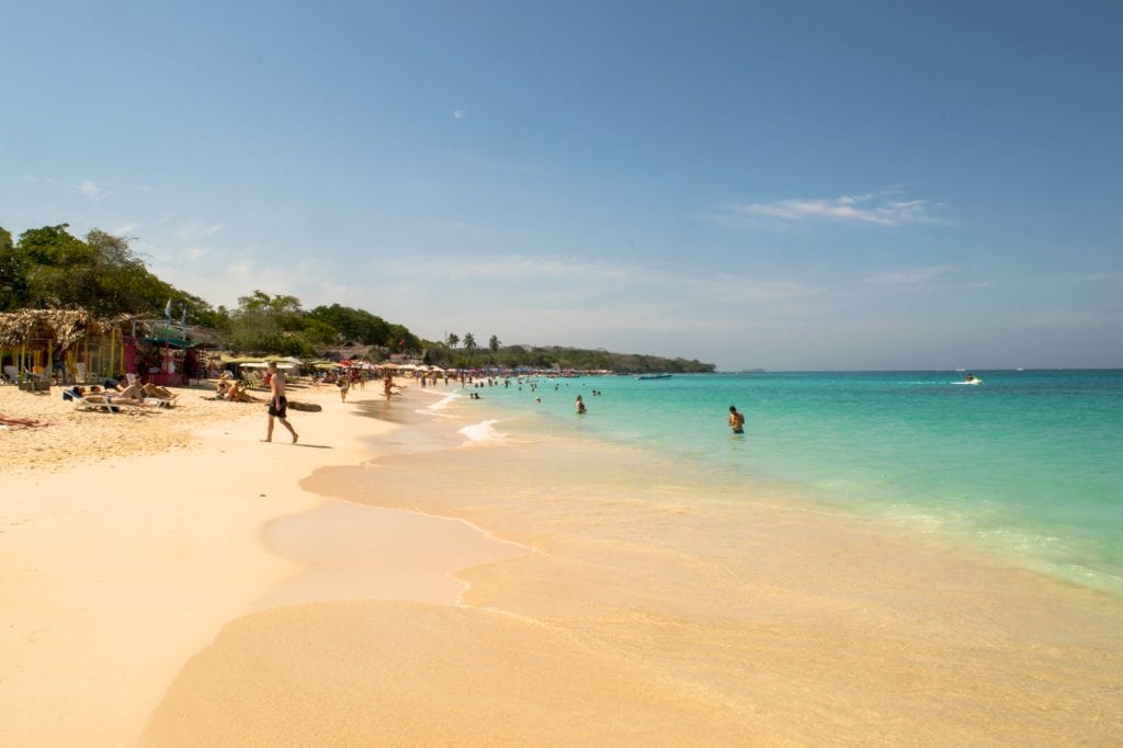 Playa Blanca in Colombia as seen looking down the beach with the turquoise sea on the right and golden sand on the left