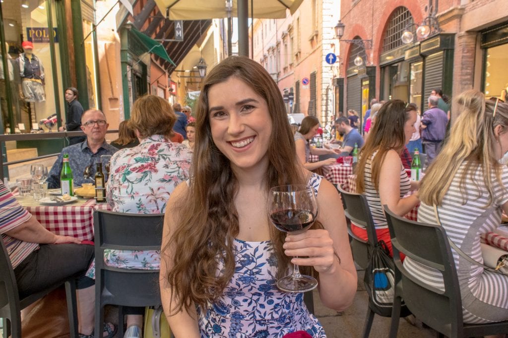 kate storm sitting at a crowded restaurant in bologna italy drinking red wine