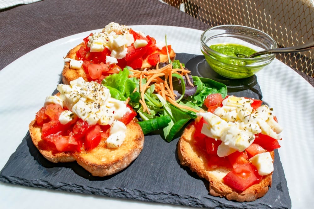 plate of 3 bruschetta slices with pesto on the side, one of the best things to eat in italy