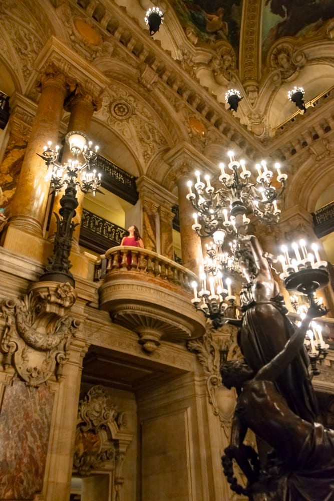 kate storm standing on a balcony in palais garnier wearing a red dress