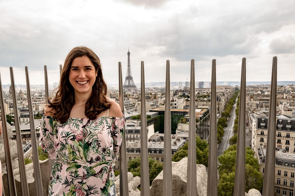 kate storm visiting arc de triomphe paris with metal spikes and eiffel tower in the background
