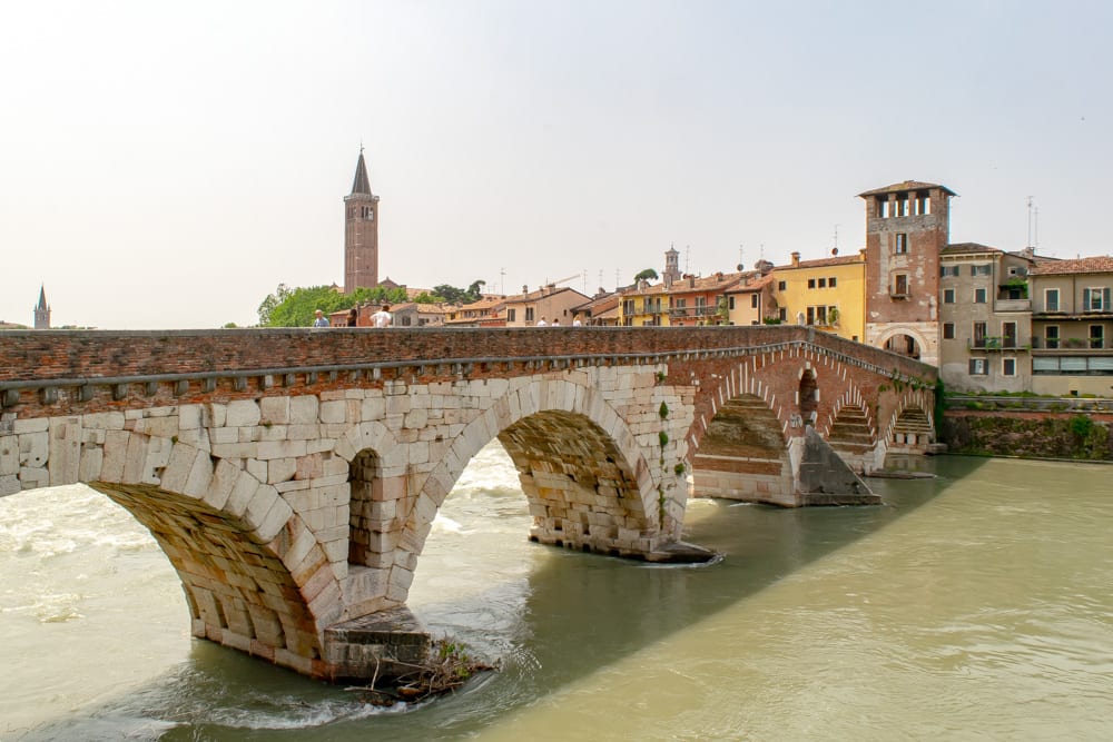 the bridge of ponte pietra crossing the adige river with verona's historic center in the background, visiting is one of the best things to do in verona italy
