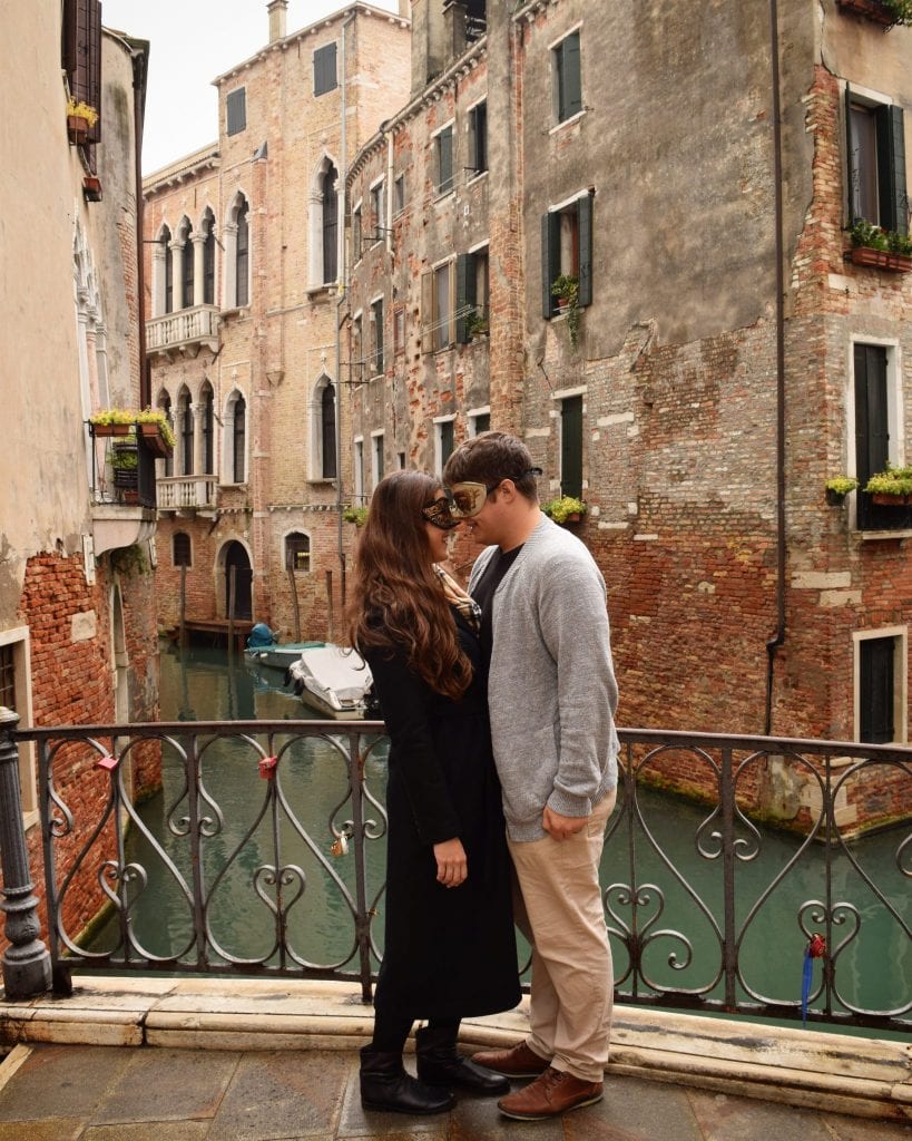 kate storm and jeremy storm wearing masks posing on a bridge in venice italy