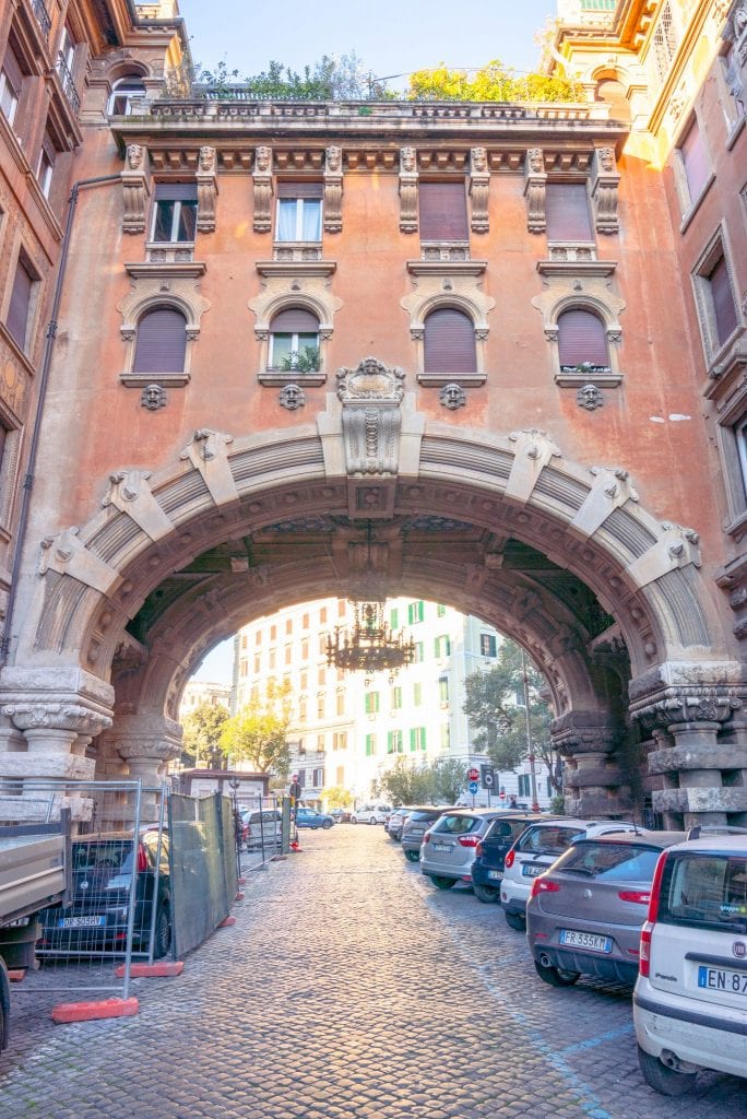 vertical photo of the entrance arch to quartiere coppede rome neighborhood with chandelier visible under arch