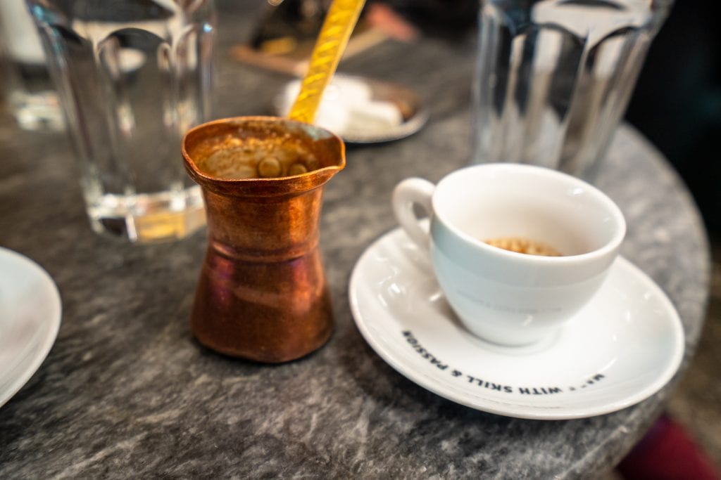 greek coffee in a white cup with a copper cup next to it