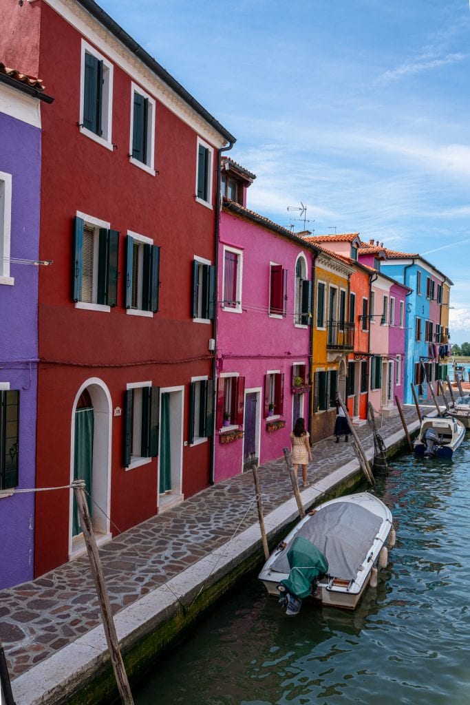 kate storm standing along a row of colorful houses in burano venice with canal to the right