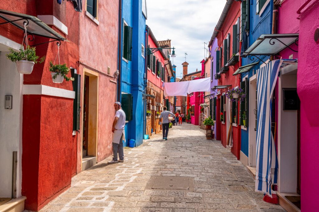 Photo of a colorful street in Burano with a man standing to the left, as seen on a trip to Burano from Venice.