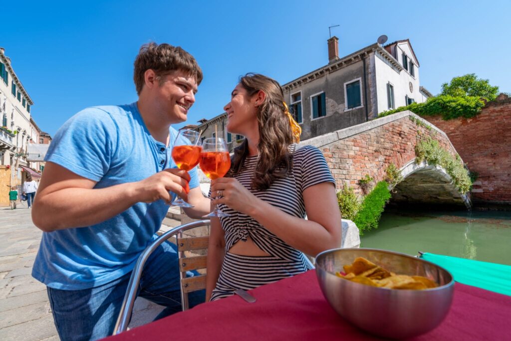 Couple toasting with Aperol Sprtize near a bridge in Cannaregio