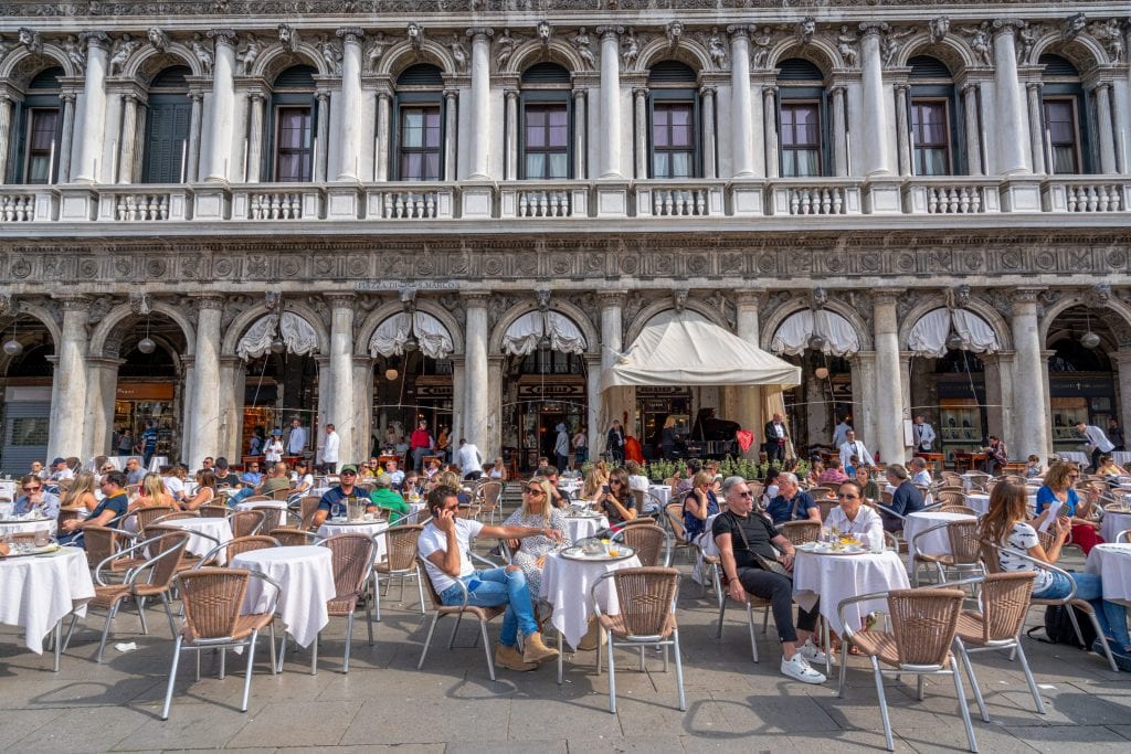tourists enjoying coffee at an outdoor cafe in famous venice square st marks, will pay coperto in italy