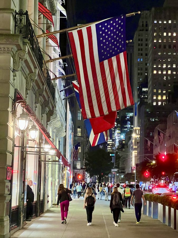 four people walking down fifth avenue at night in new york city with flags hanging above their heads