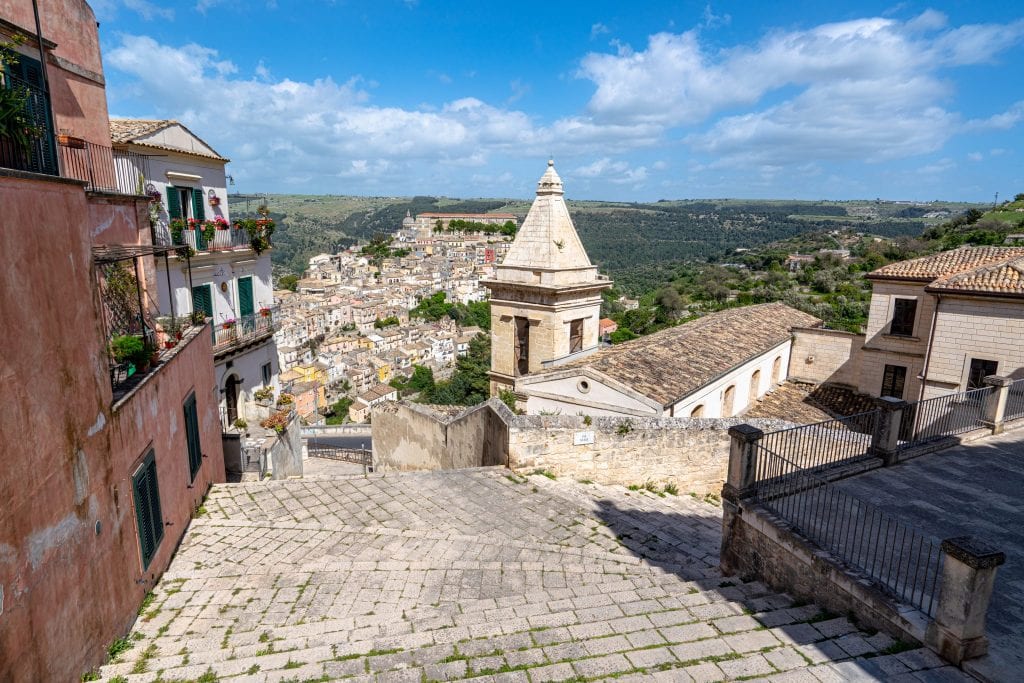 Steep staircase in Ragusa with a church tower on the right and Ragusa Ilba visible in the distance