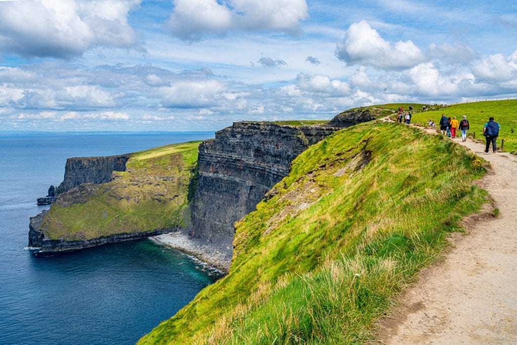 People hiking along the Cliffs of Moher Coastal Walk near Doolin Ireland, a small beach is visible on the left