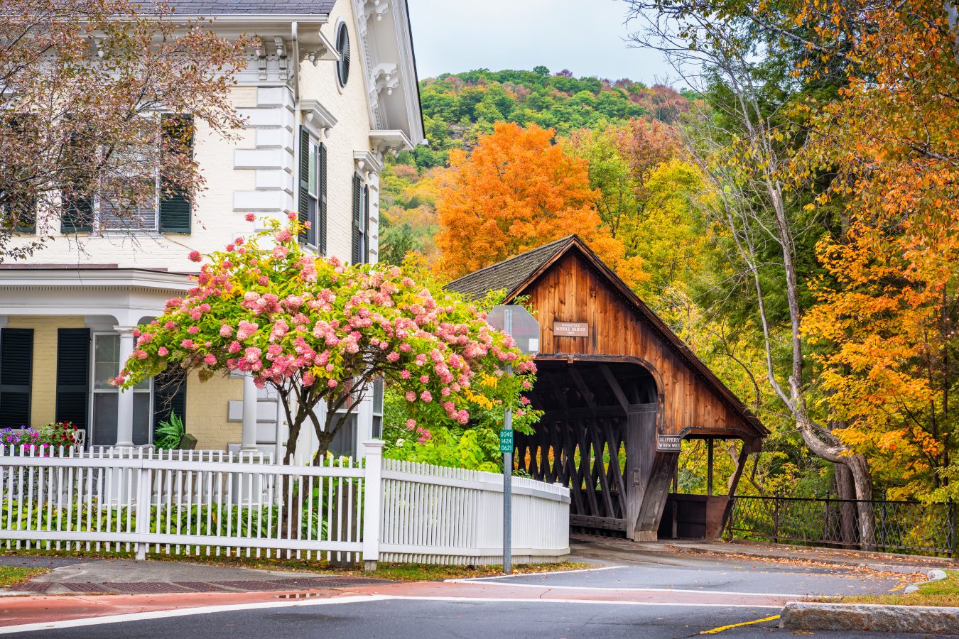 woodstock vermont in early fall with white home in the foreground and entrance to covered bridge in the background