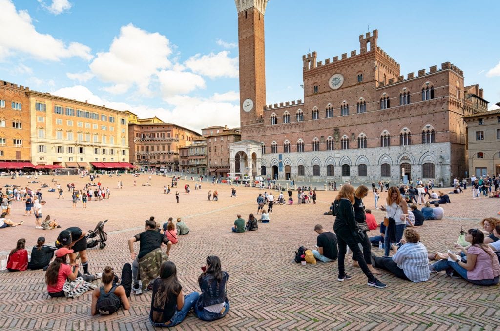 collection of people hanging out in piazza del campo with palazzo pubblico siena in the background