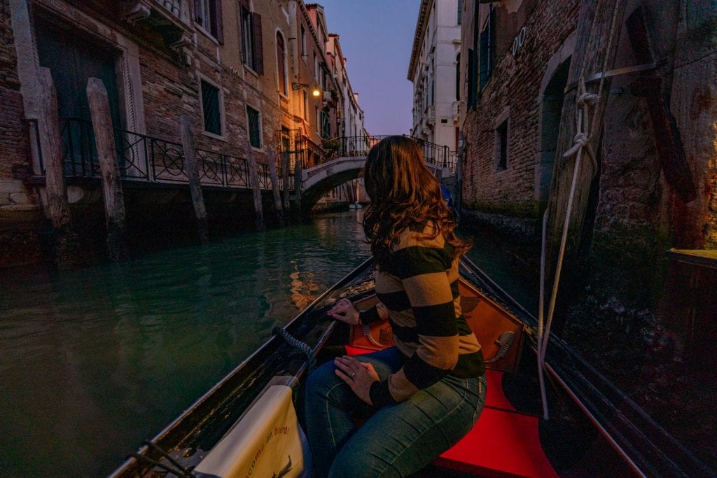 Kate Storm sitting in a gondola at night looking away from the camera. A nighttime gondola ride is one of the best things to do in Venice at night!