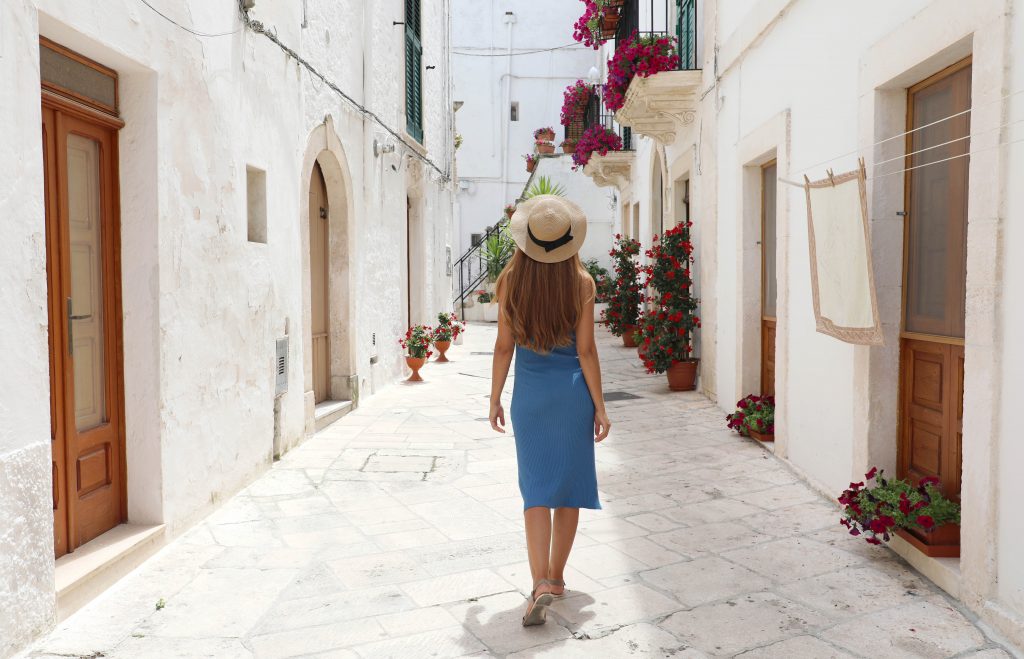 young woman in a blue dress walking along a whitewashed street in Locorotondo, one of the best italian villages to visit