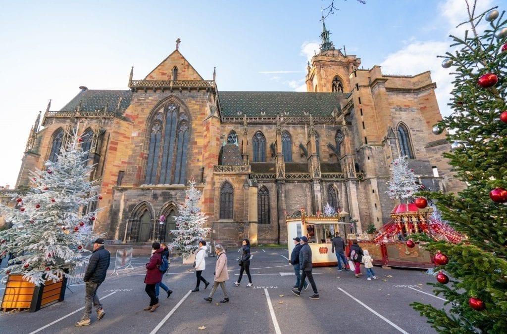 Church in Colmar in winter with Christmas trees and children's ride set up in front of it