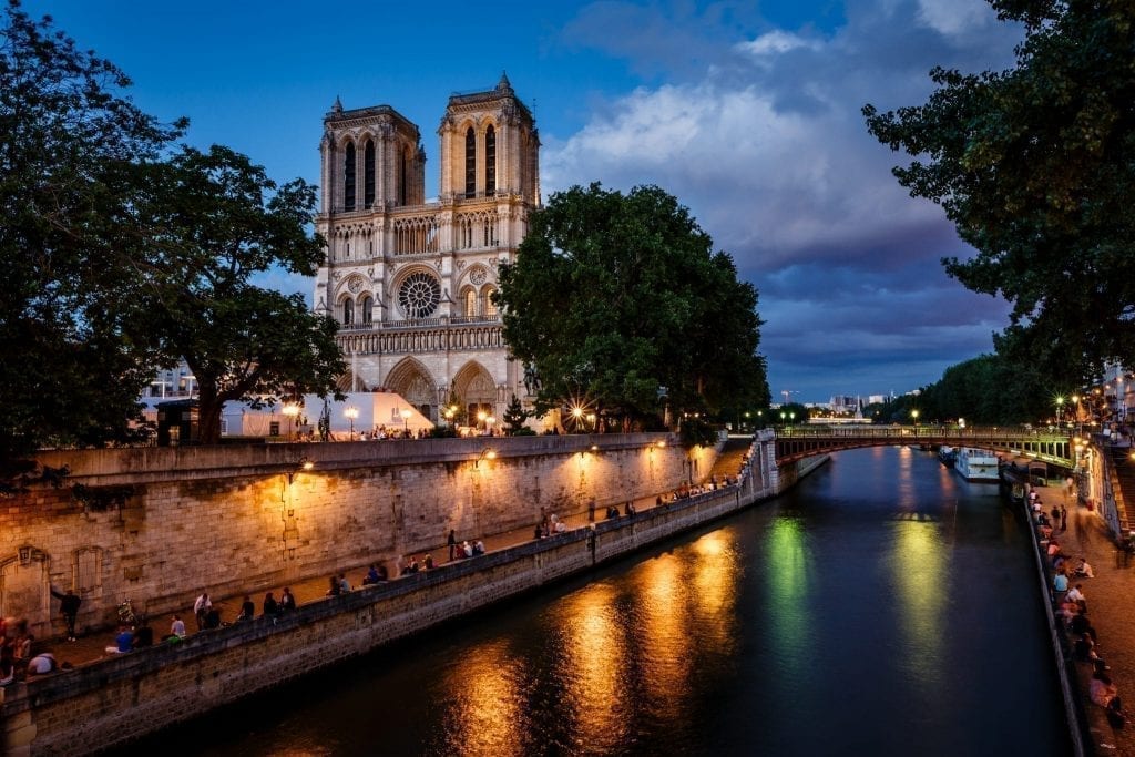 Seine River in Paris at night with Notre Dame visible on the left. Strolling along the Seine is one of the most classic things to do in Paris at night.