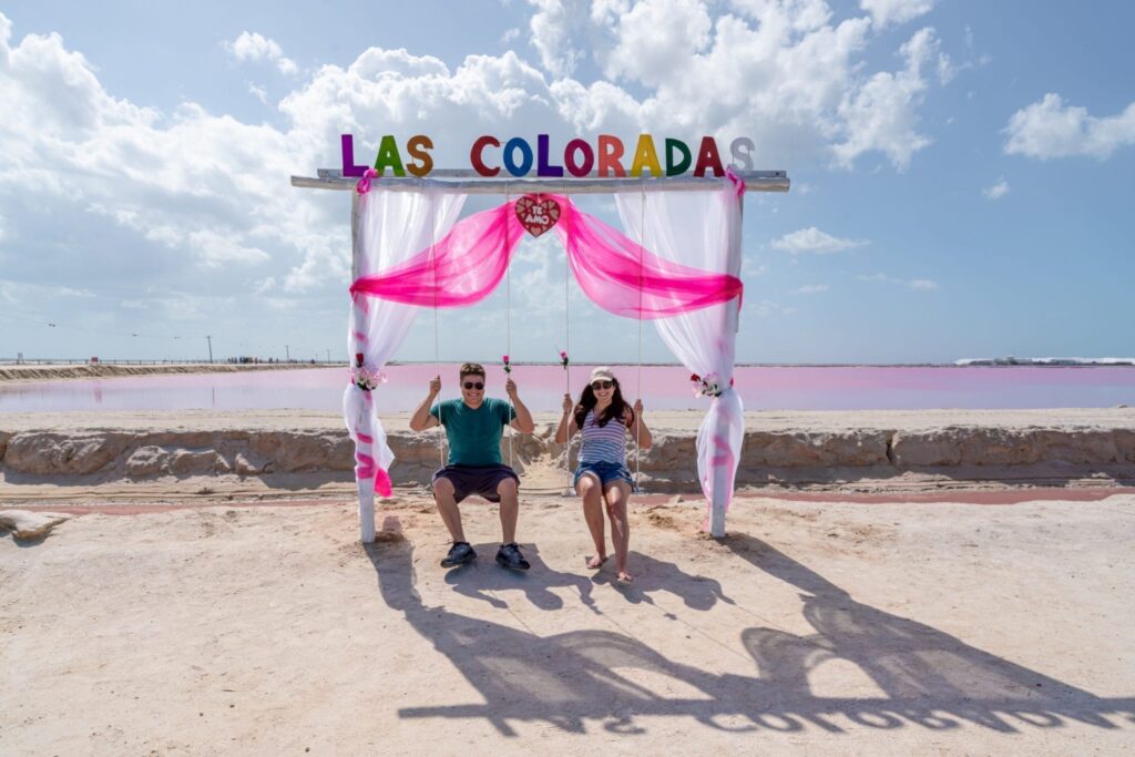 Kate Storm and Jeremy Storm sitting in swings in front of the pink lakes las coloradas mexico