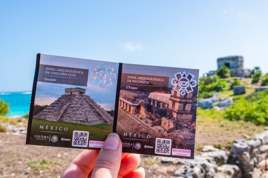 ticket for tulum ruins being held out in front of the beach, a fun travel souvenir collection idea
