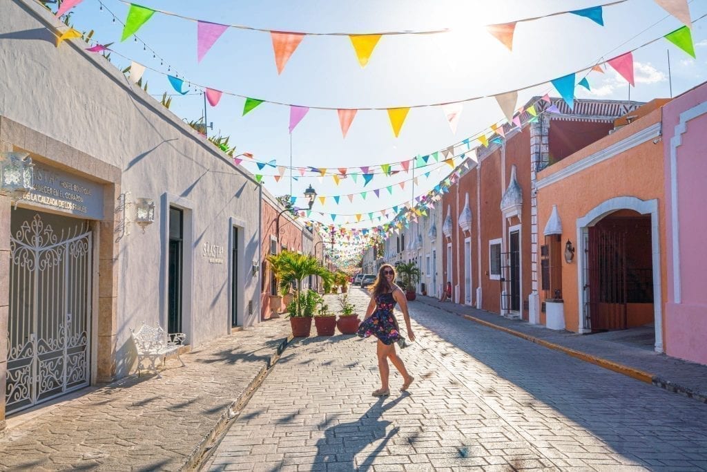 Kate Storm standing on a colorful street with flags hanging over it in Valladolid Mexico during a Yucatan road trip