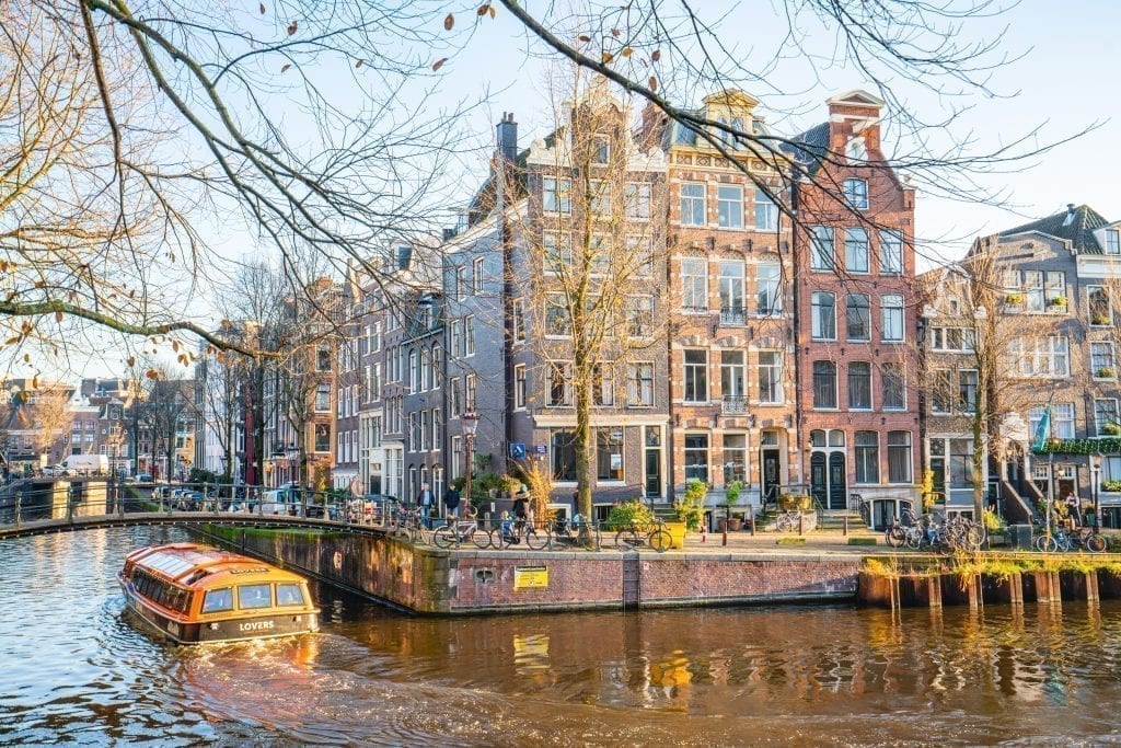 Canal boat floating through Amsterdam as it turns a corner. Typical Dutch houses visible in the background