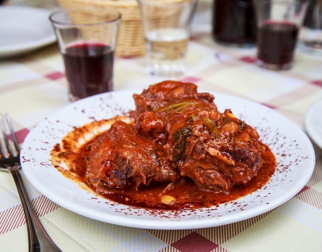 Coda alla vaccinara on a white plate set on a checkered tablecloth--definitely a dish to consider when deciding what to eat in Rome