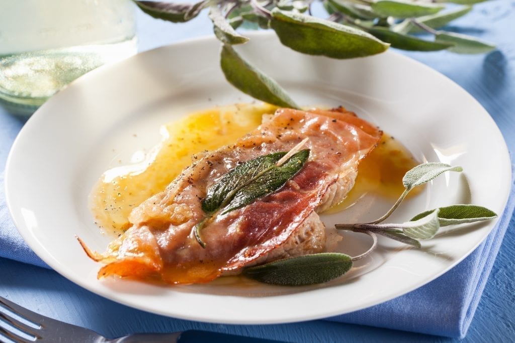 Saltimbocca on a white plate with bay leaves in the background