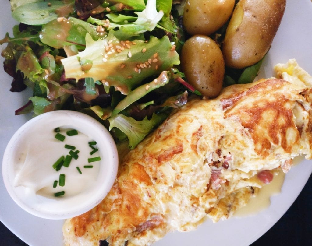 French omelet on a white plate with a side of salad and roasted potatoes. Omelets are not a typical French breakfast food!