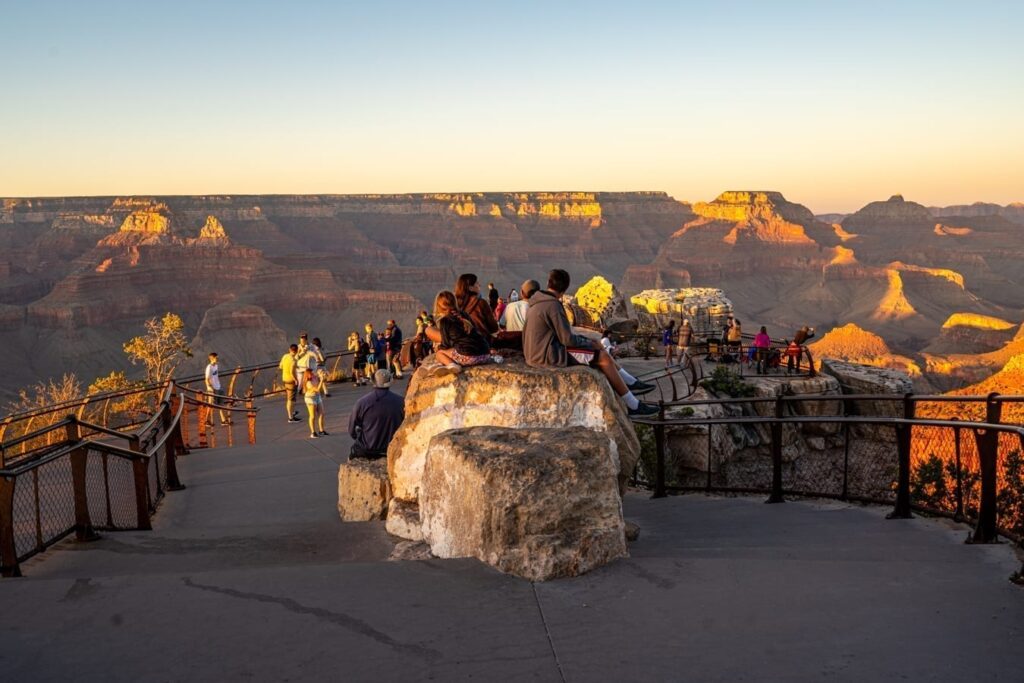a crowd of people watching the sunset at mather point near grand canyon rim trail