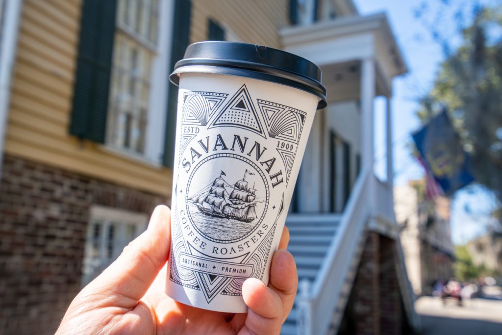 cup from savannah coffee roasters, one of the best coffee shops savannah ga, being held up in front of yellow building