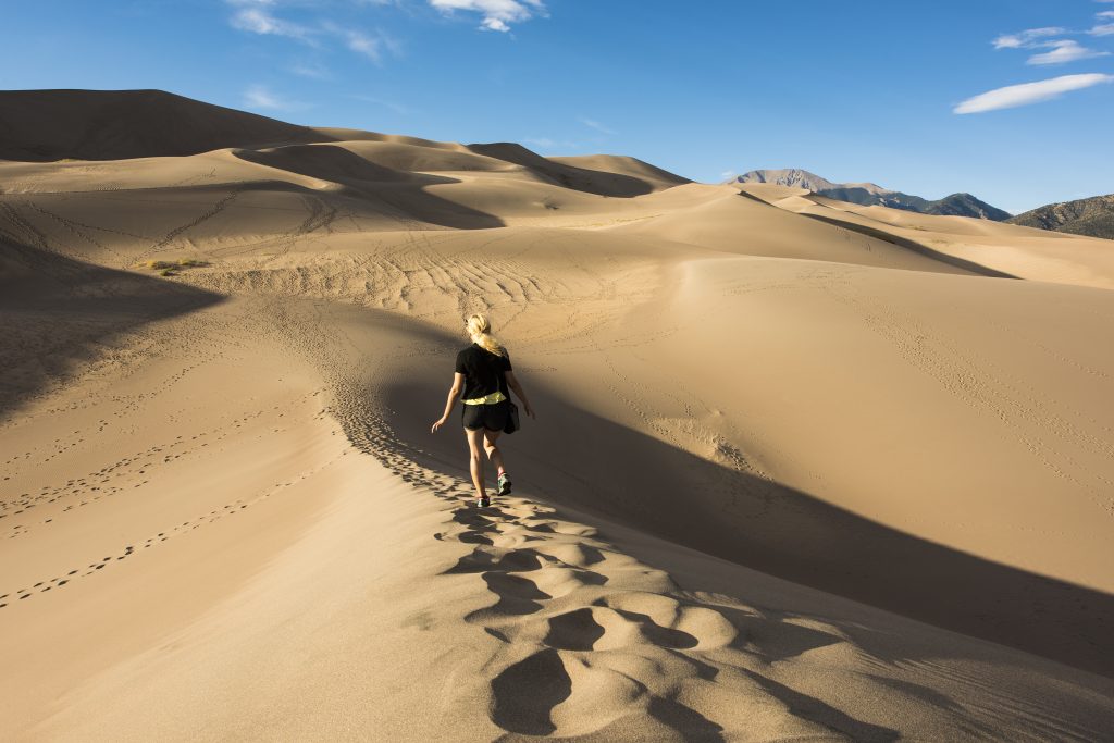 young woman hiking on a sand dune in great sand dunes national park, a bucket list colorado travel destinations