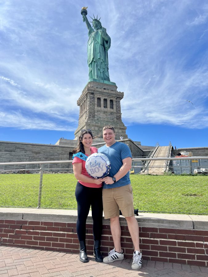 kate storm and jeremy storm holding "it's a boy" balloon in front of the statue of liberty, a fun nyc babymoon idea
