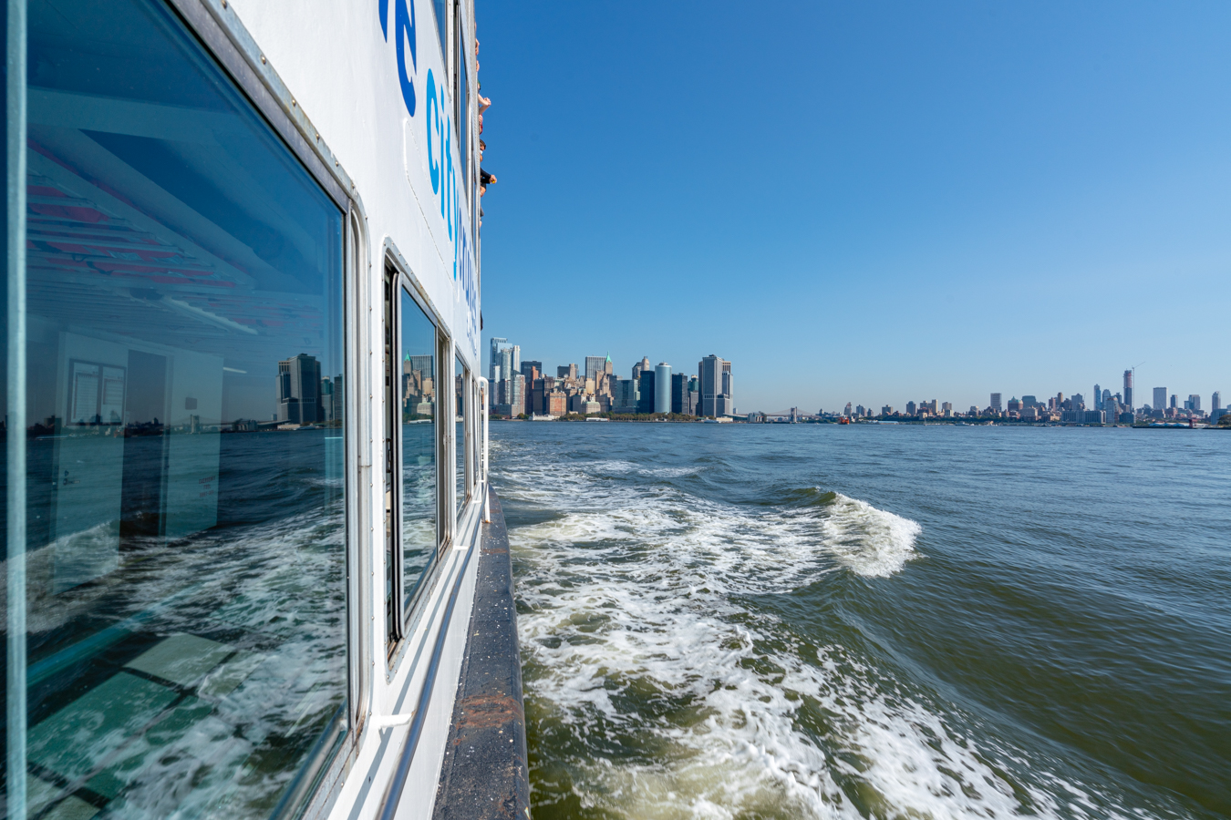 statue of liberty and ellis island ferry with views of manhattan in the distance