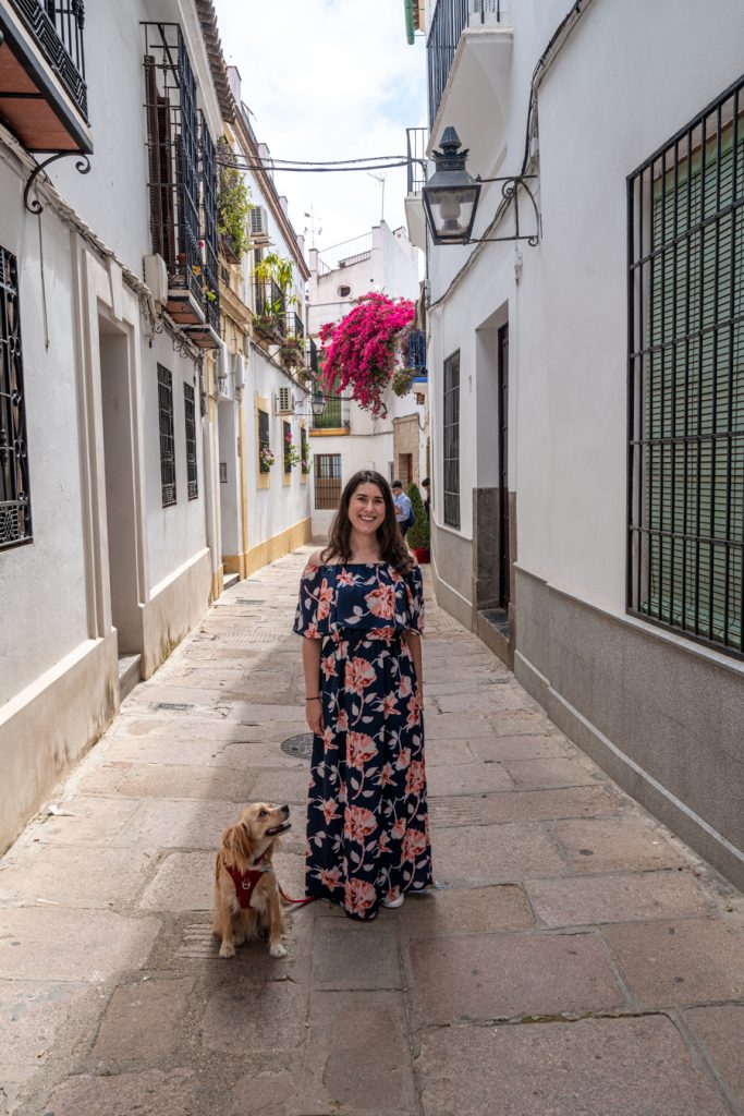 kate storm wearing a floral dress with her dog ranger storm on a stone street between white buildings when visiting cordoba spain during spring in europe