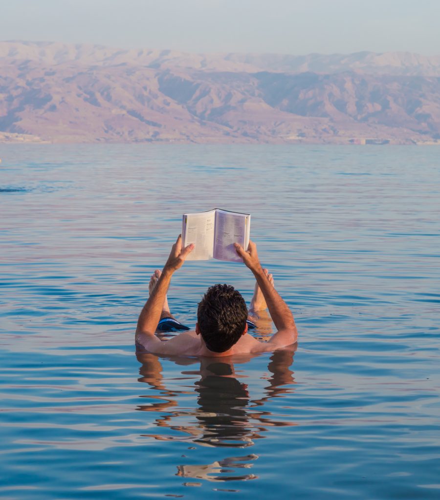 man floating in dead sea jordan while holding up a book