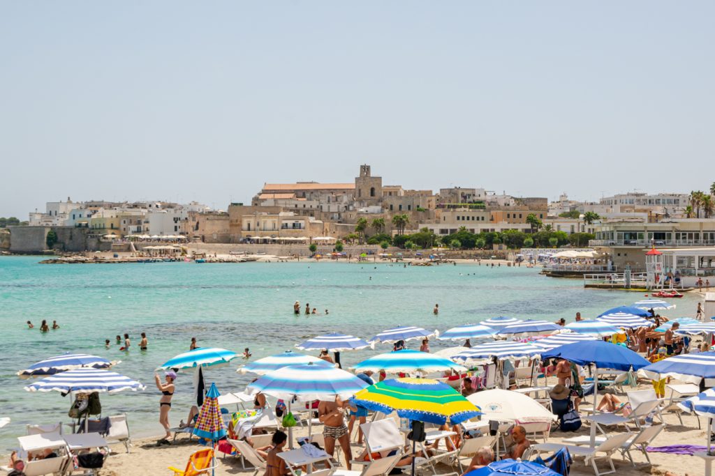 collection of colorful beach umbrellas in the foreground with water and otranto italy in the background