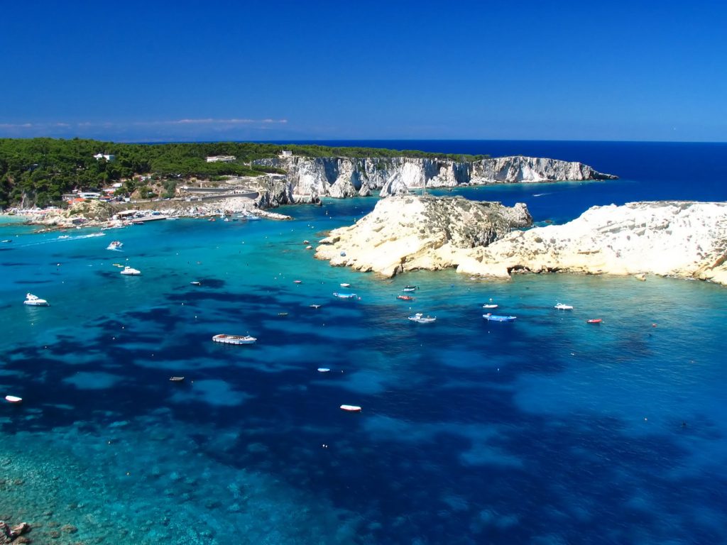 view of white cliffs, bright blue water and sailboats from above on tremiti islands