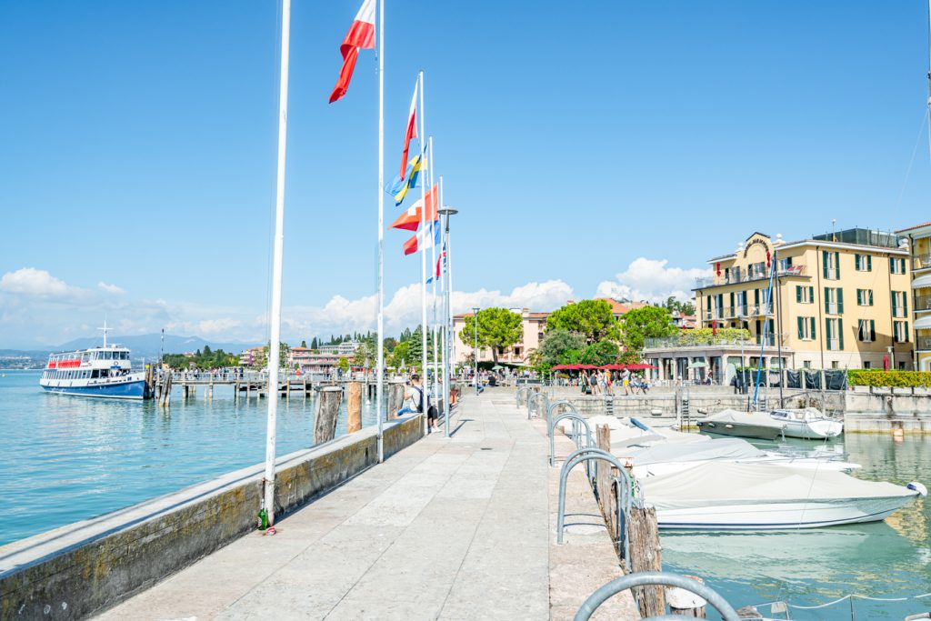 promenade along the water in sirmione lake garda with flags on the left side
