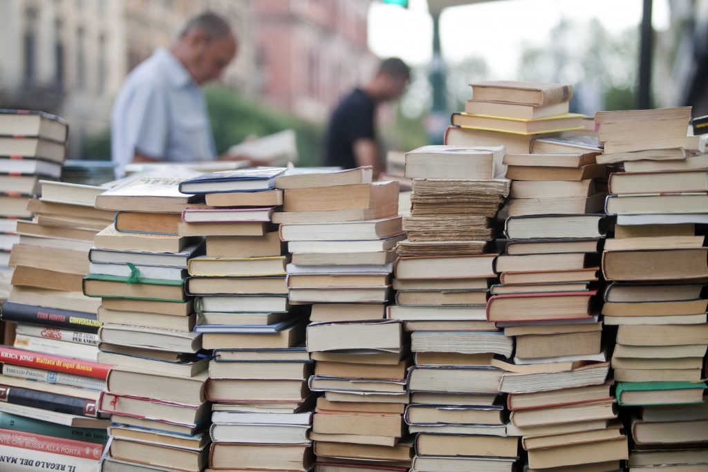 pile of books for sale as things to buy in rome italy, two men reading in the background