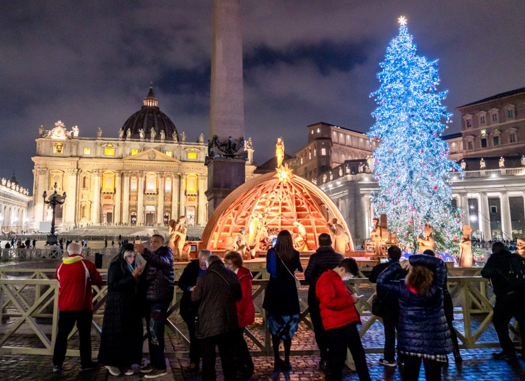christmas decorations in st peters square being admired by visitors during december in rome at night