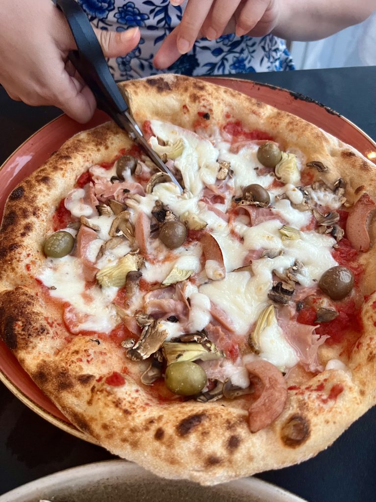 kate storm slicing a capricciosa traditional italian pizza with scissors